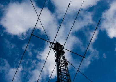 A tall communication tower with multiple antennas extends into a blue sky dotted with scattered clouds. The structure's lattice frame is clearly visible against the sky.